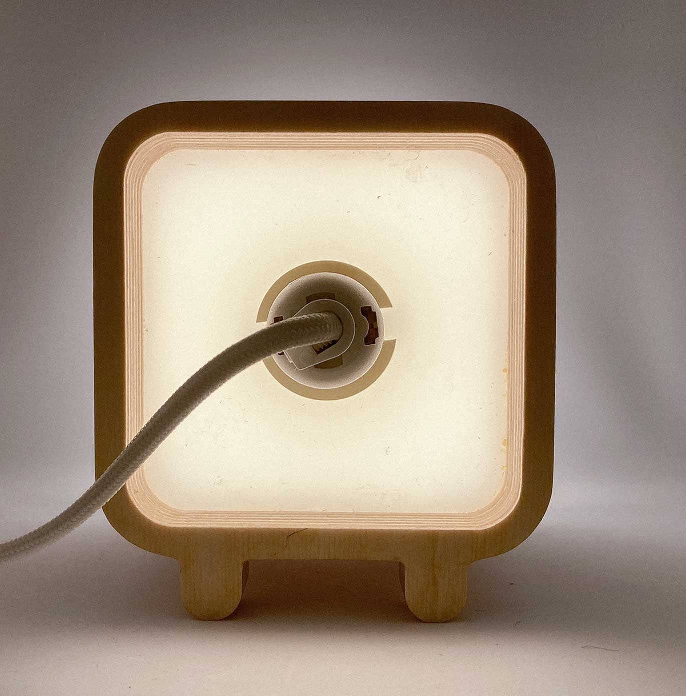 The back of a Lampun box, socket and cord visible, plywood glowing warm from the light inside